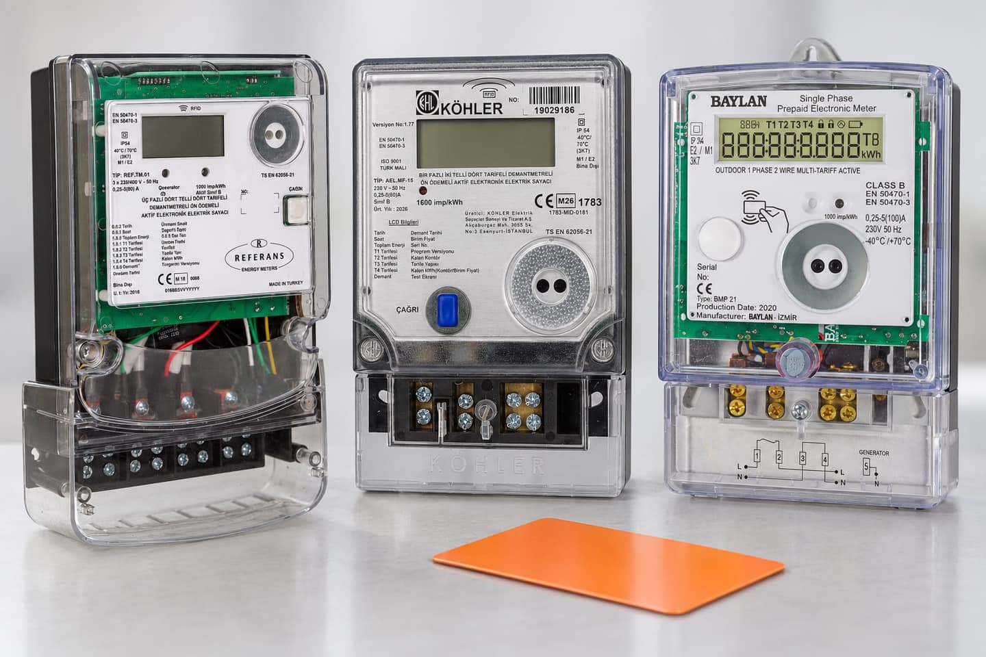 Three prepaid electricity meters side by side: Referans, Köhler MF15 and Baylan BMP 21, with an orange card in front